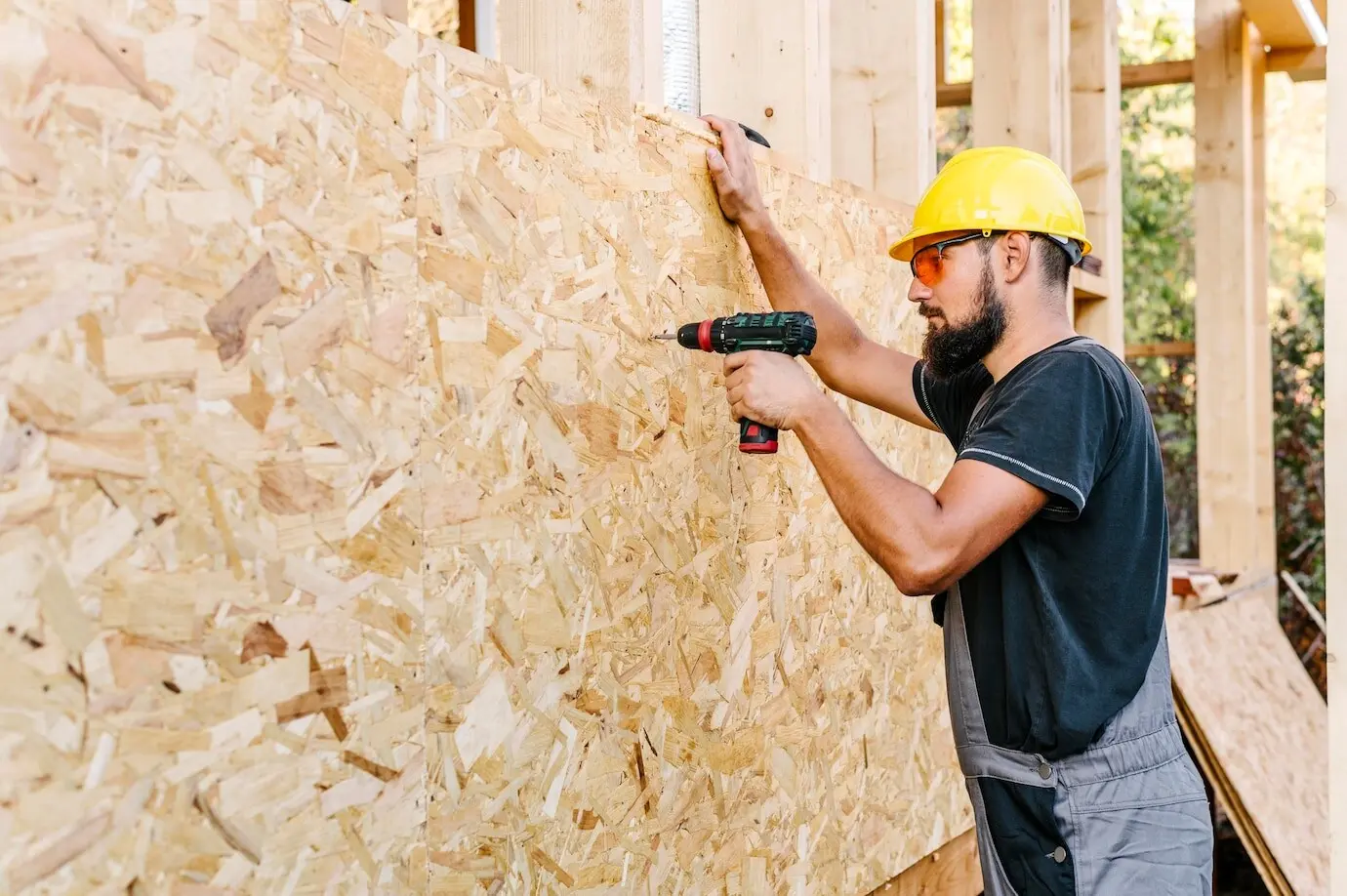 Profile view of a construction worker drilling into plywood with copy space